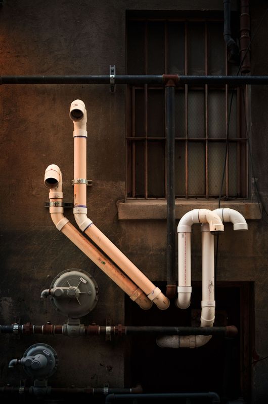 Weathered wall with exposed copper and white PVC pipes in an industrial setting