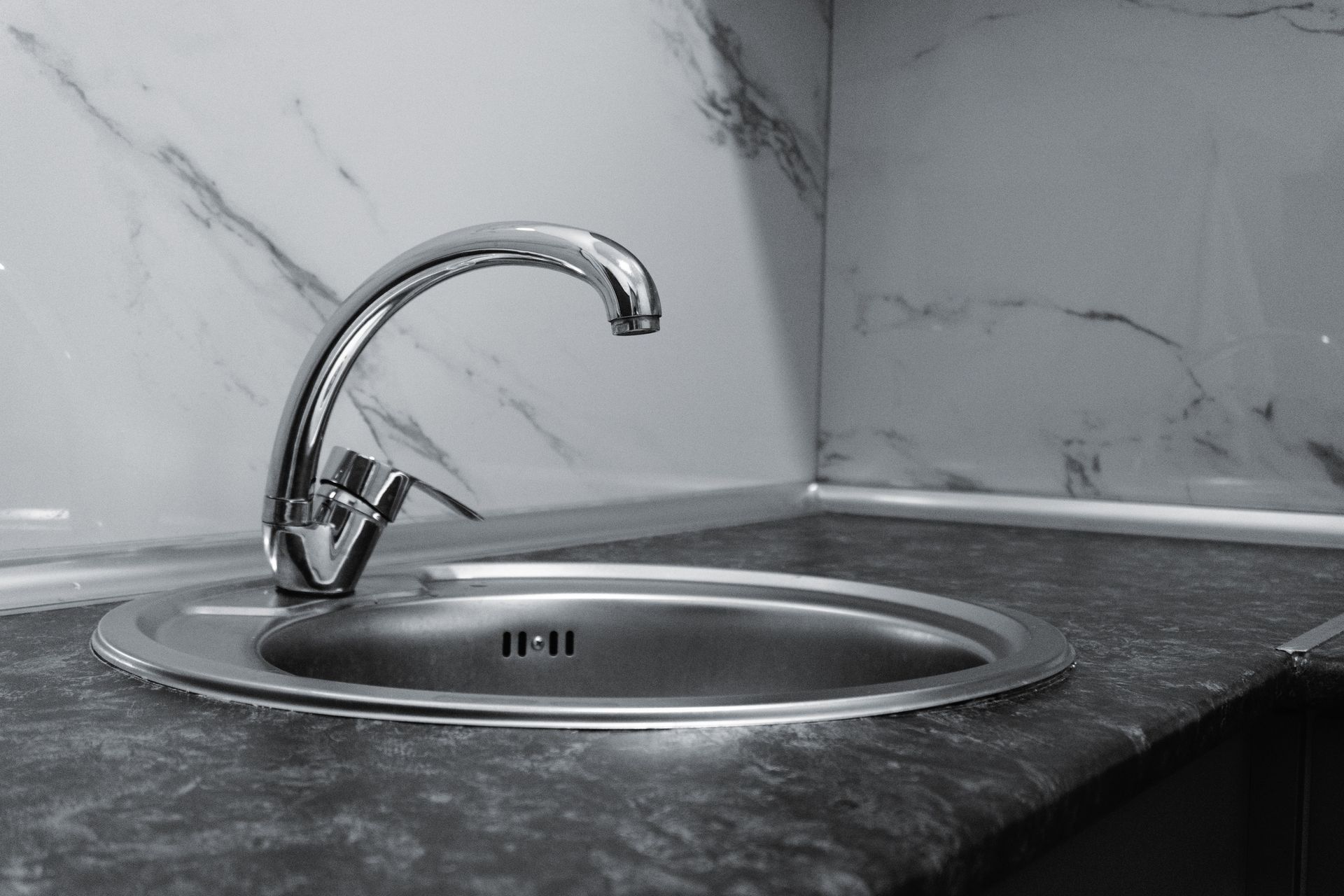 Chrome faucet over a stainless steel sink in a gray marble kitchen countertop