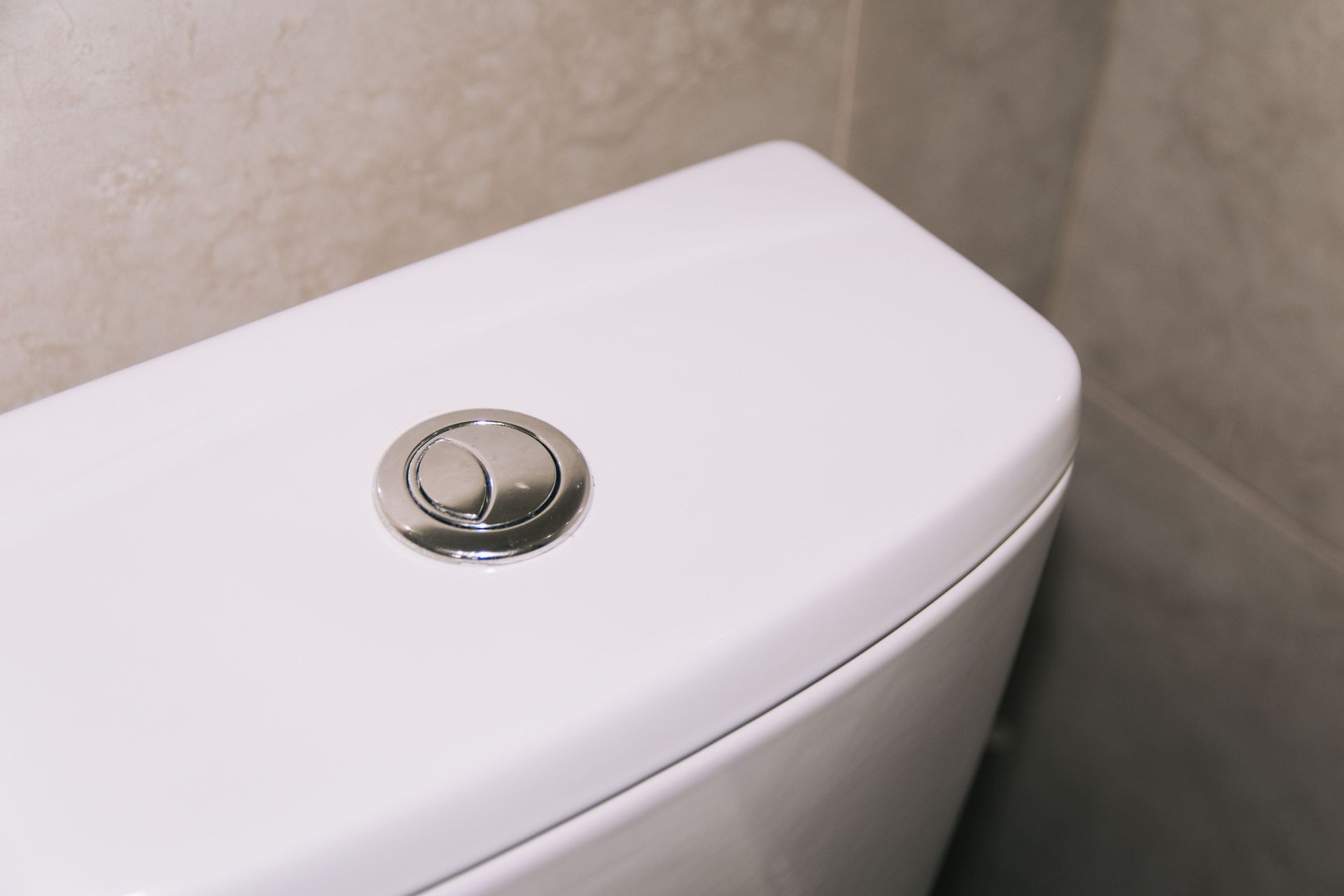 White toilet tank with a chrome dual-flush button on a bathroom wall.