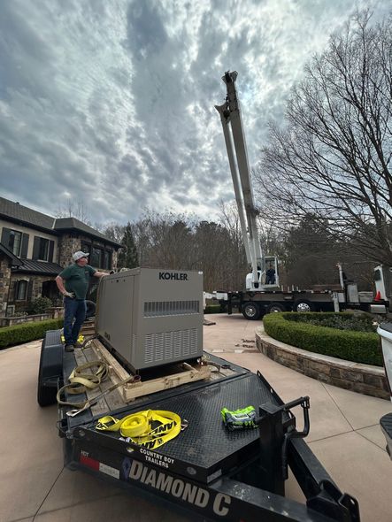 Workers beside a crane on a flatbed trailer in a residential street under a cloudy sky