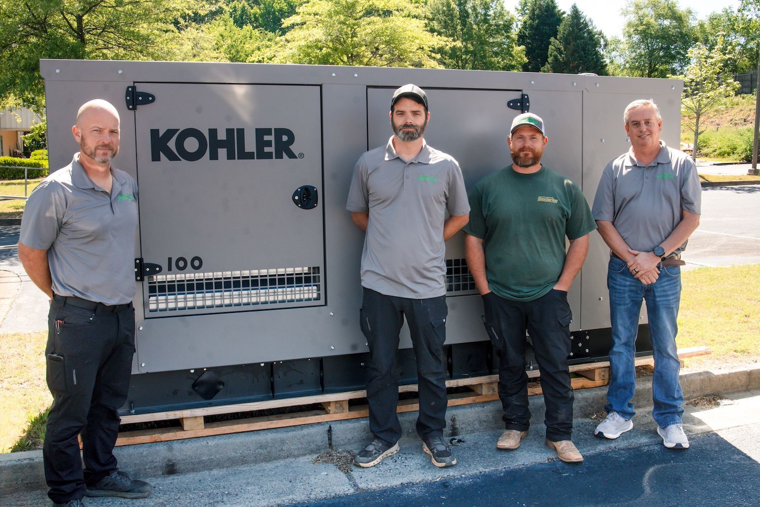 Four people standing beside a Kohler generator outdoors on a sunny day