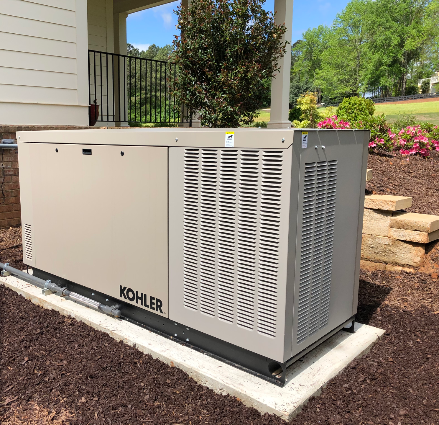 Kohler backup generator beside a house, on a concrete pad in a landscaped yard