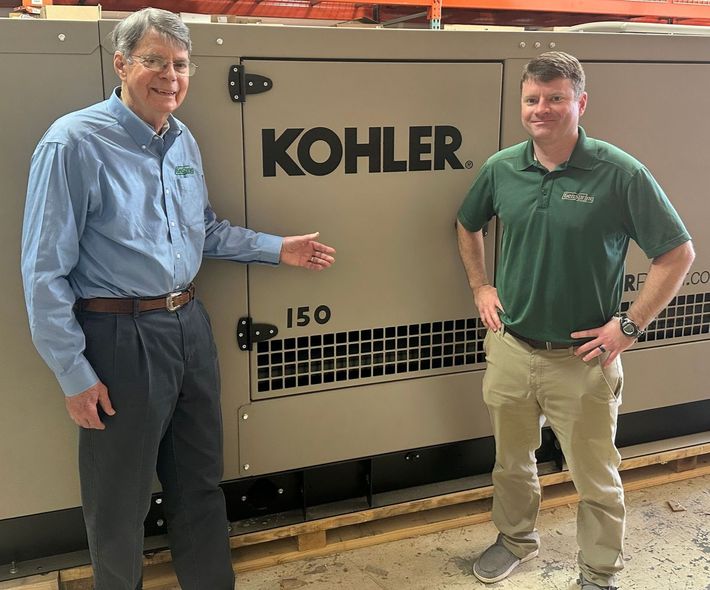 Two men standing beside a large Kohler generator in an industrial setting