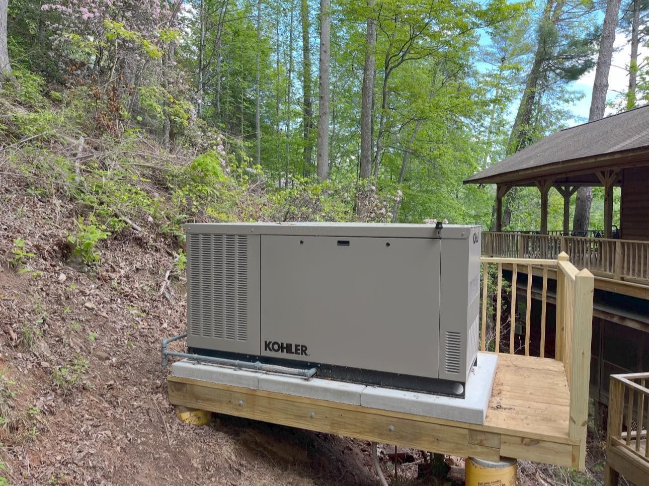 Gray Kohler generator on a wooden deck beside a house in a wooded yard