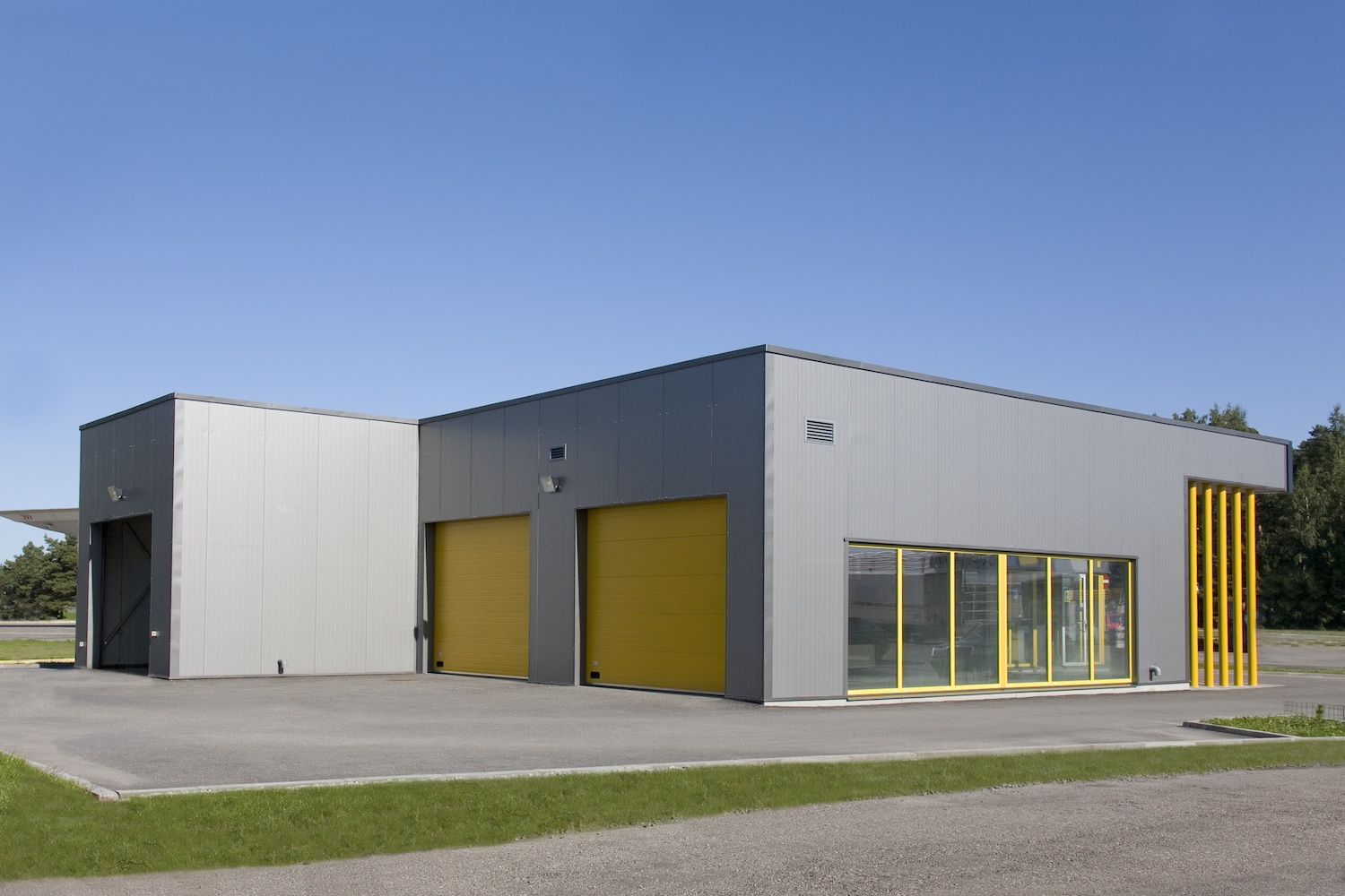 Modern gray industrial building with yellow garage doors and windows on a sunny day