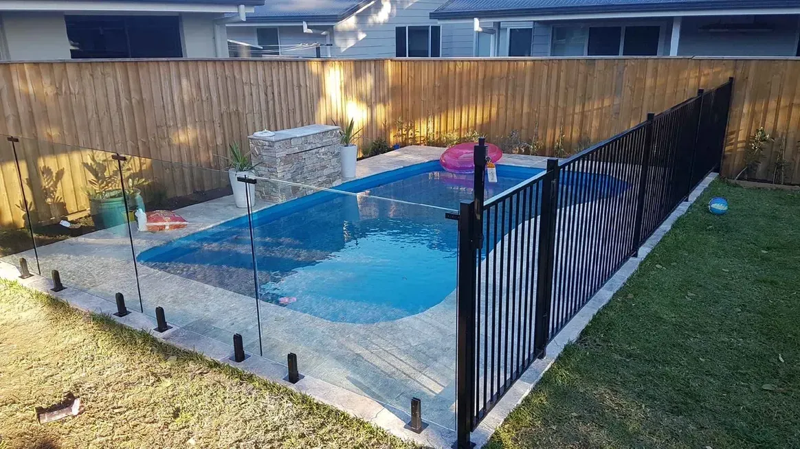 Backyard pool surrounded by black fence and a wooden fence, with blue water, and a pink floatie.