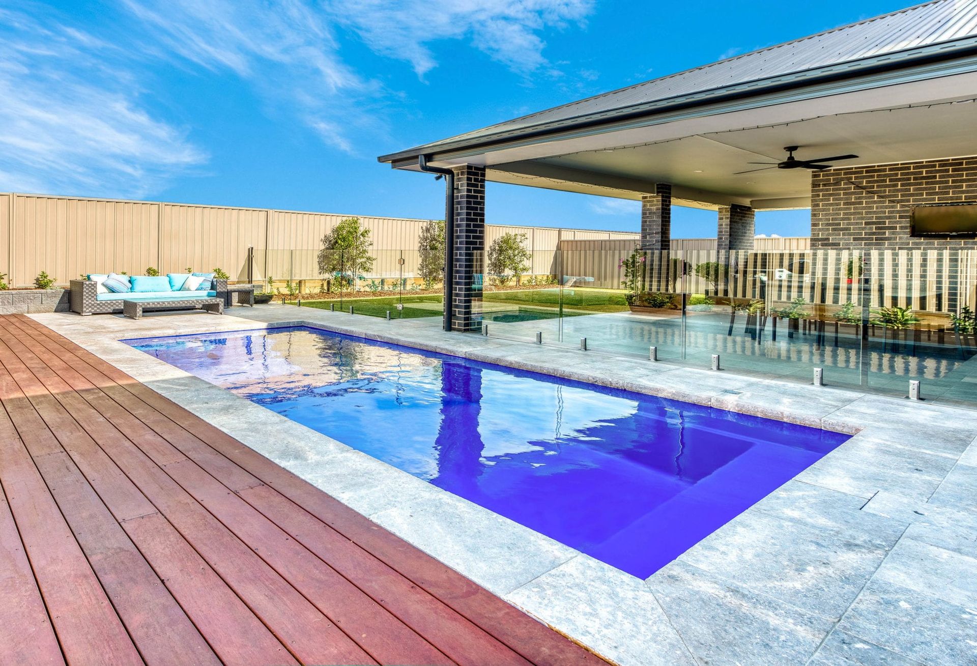 Rectangular blue pool with patio and outdoor lounge area, sunny day.