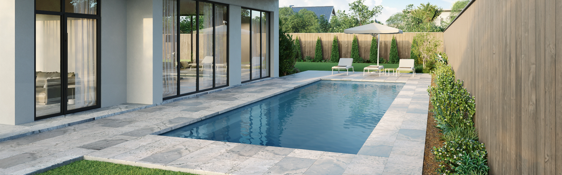 Outdoor pool with modern house, stone patio, lounge chairs, and wooden fence.