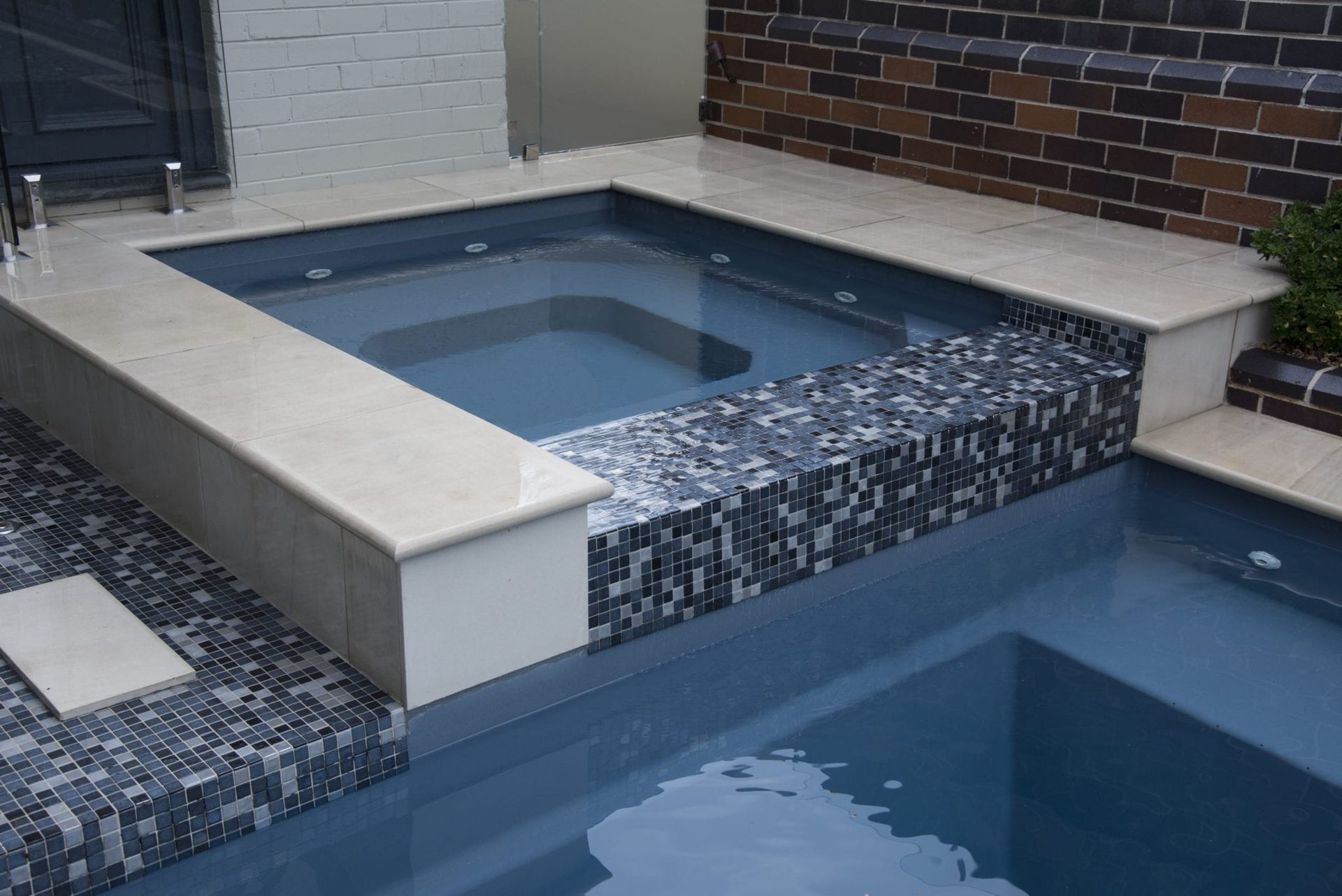 A tiled spa with two levels of water, next to a brick wall.