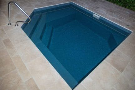 Small, square swimming pool with steps, handrail, and blue water, surrounded by beige tile.