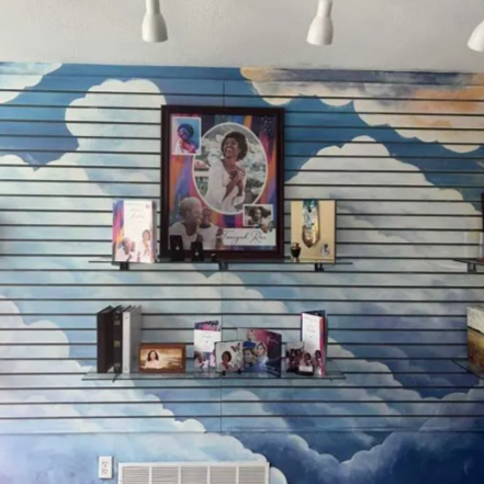 Shelves with framed photos and a mural of blue clouds painted on a slatted wall.