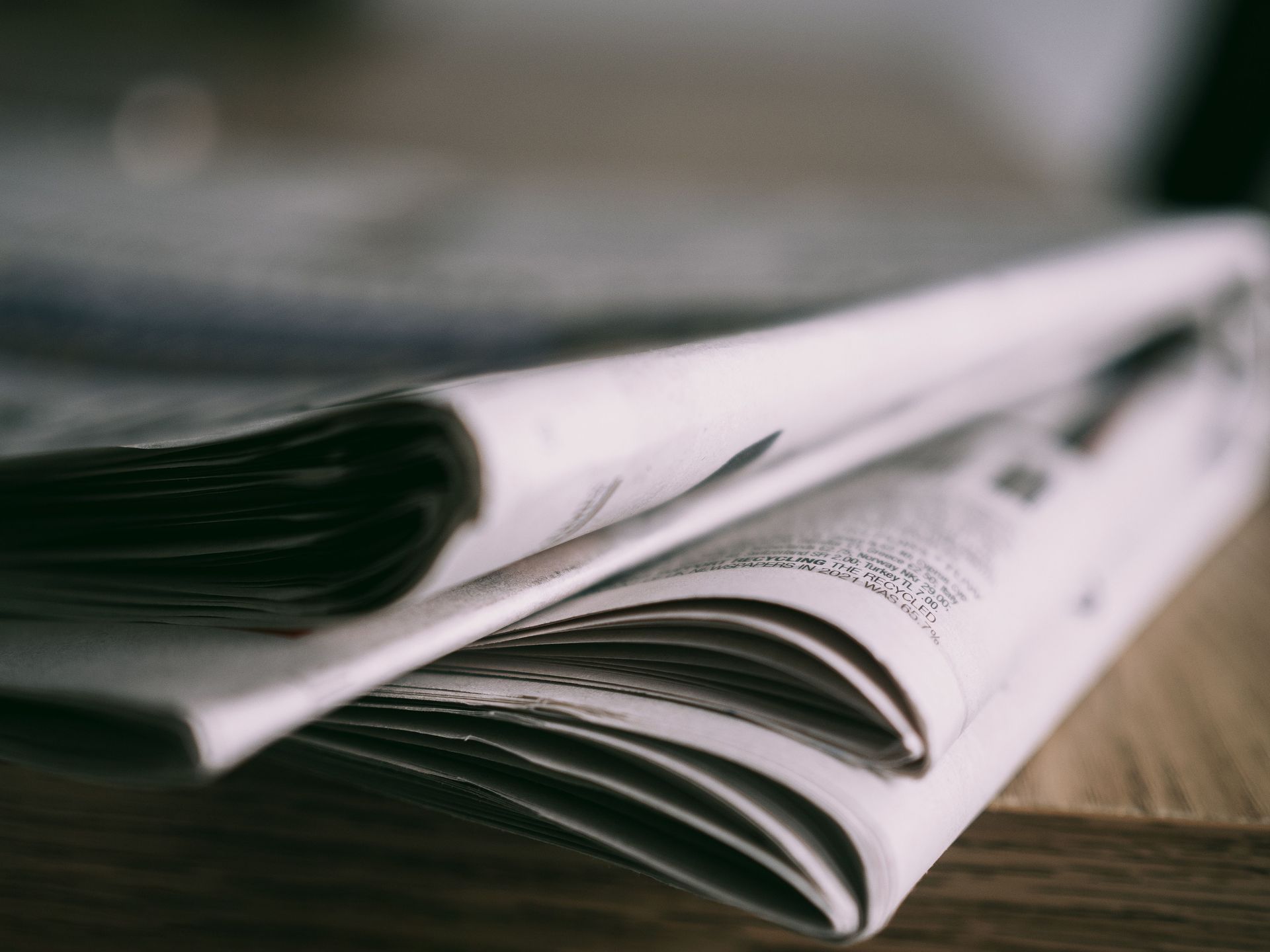 Stack of folded newspapers on a wooden surface, in soft focus.