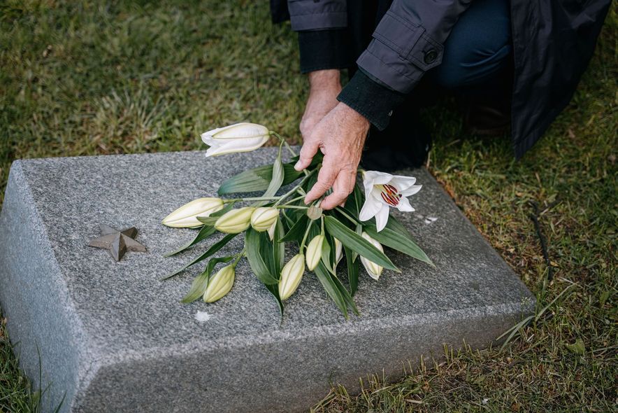 Person places white lilies on a gravestone outdoors.