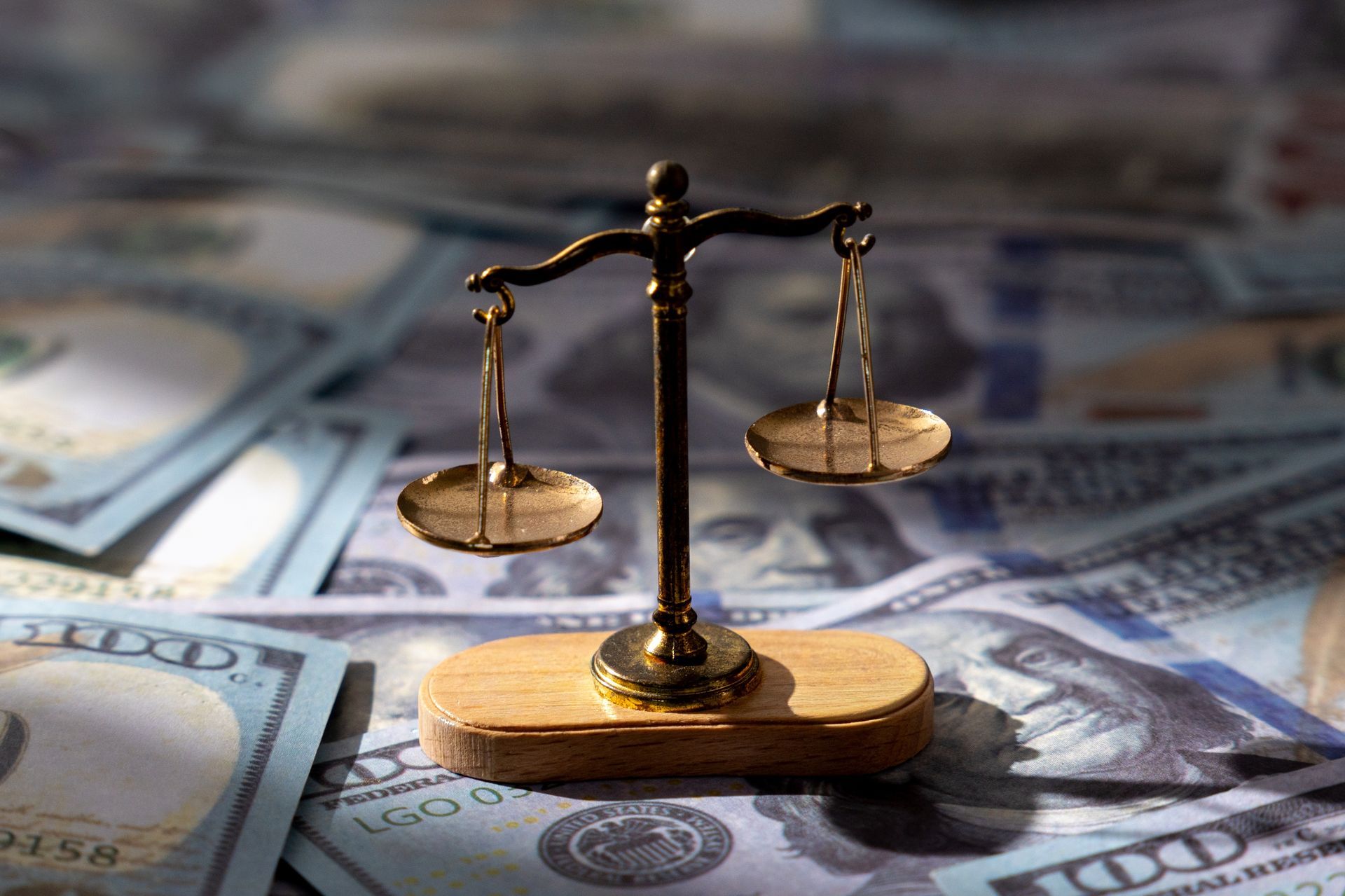 Balance scale on a wooden base atop scattered U.S. dollar bills.