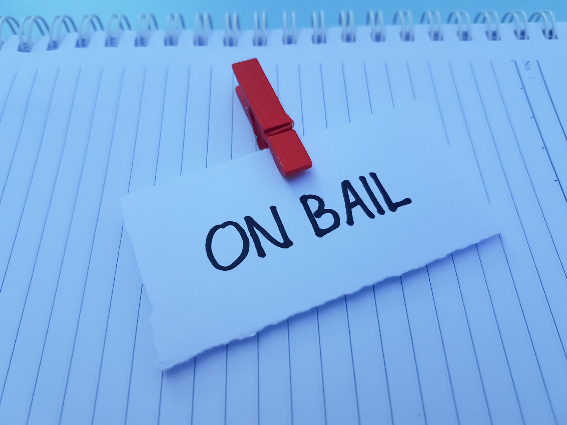 Red clothespin holds a note reading “ON BAIL” on lined paper