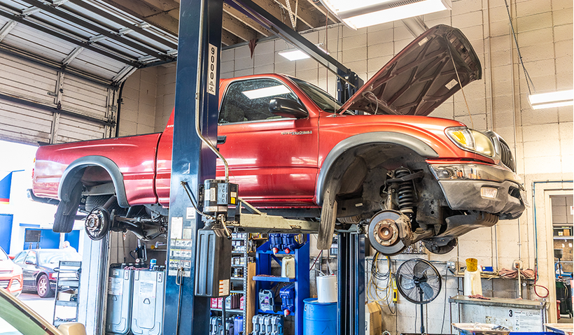 Red truck on a lift with the hood open in an auto repair shop.