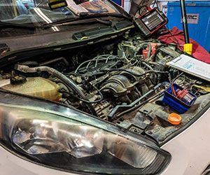 Car engine bay open for service, tools and diagnostic equipment present. White car.