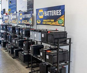 NAPA Batteries display at a store, black racks with many car batteries. Sign reads 