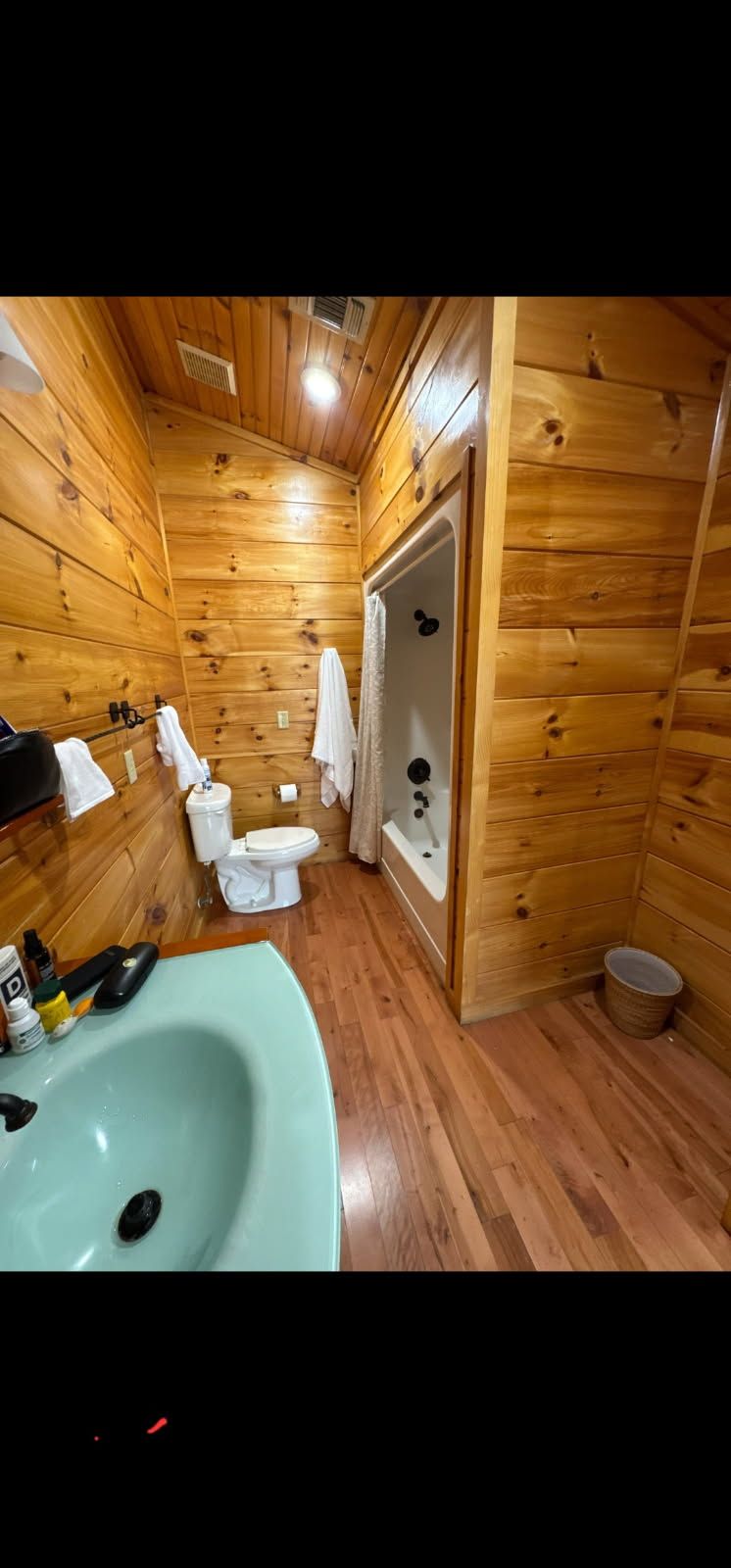 Wood-paneled bathroom with toilet, shower, sink, and wood floor, viewed from the doorway