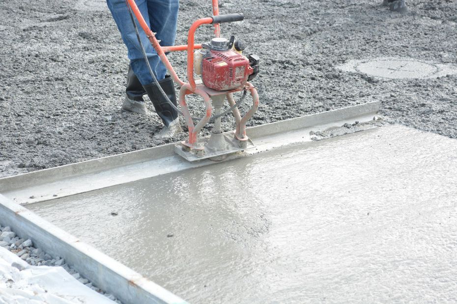 Worker using a red concrete screed to level wet gray concrete on a construction site