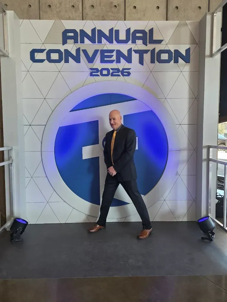 Person posing onstage in front of an “Annual Convention 2025” backdrop with a blue circular logo.
