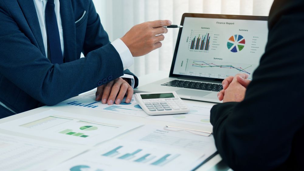 Two people reviewing charts and graphs on a laptop during a business meeting