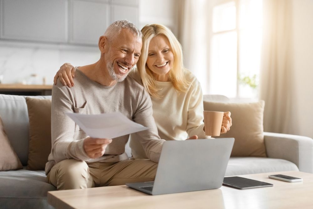 Couple reviewing a document beside a laptop in a bright living room