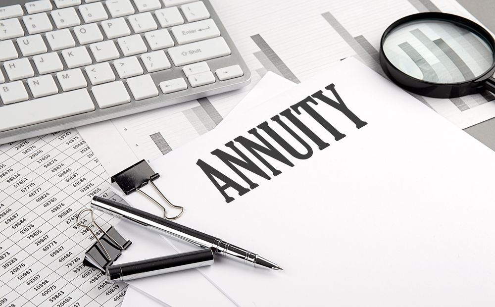 Documents and calculator beside the word “ANNUITY” on a desk, with a magnifying glass and keyboard nearby