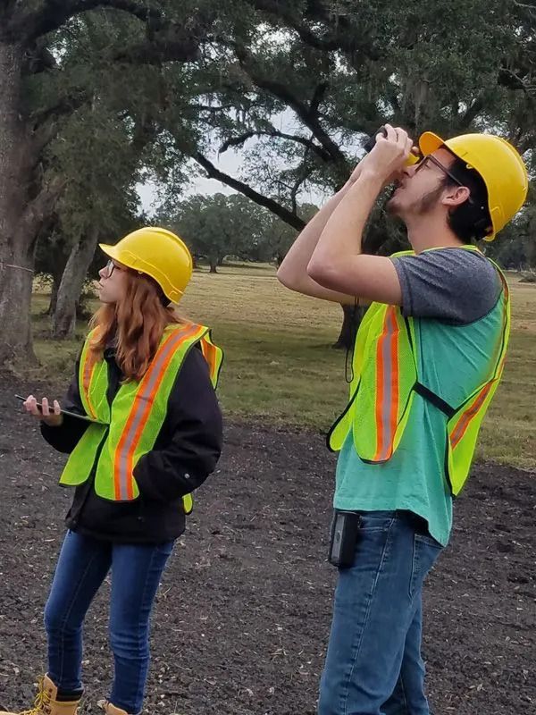 Two workers in hard hats and safety vests looking up outdoors on a worksite.