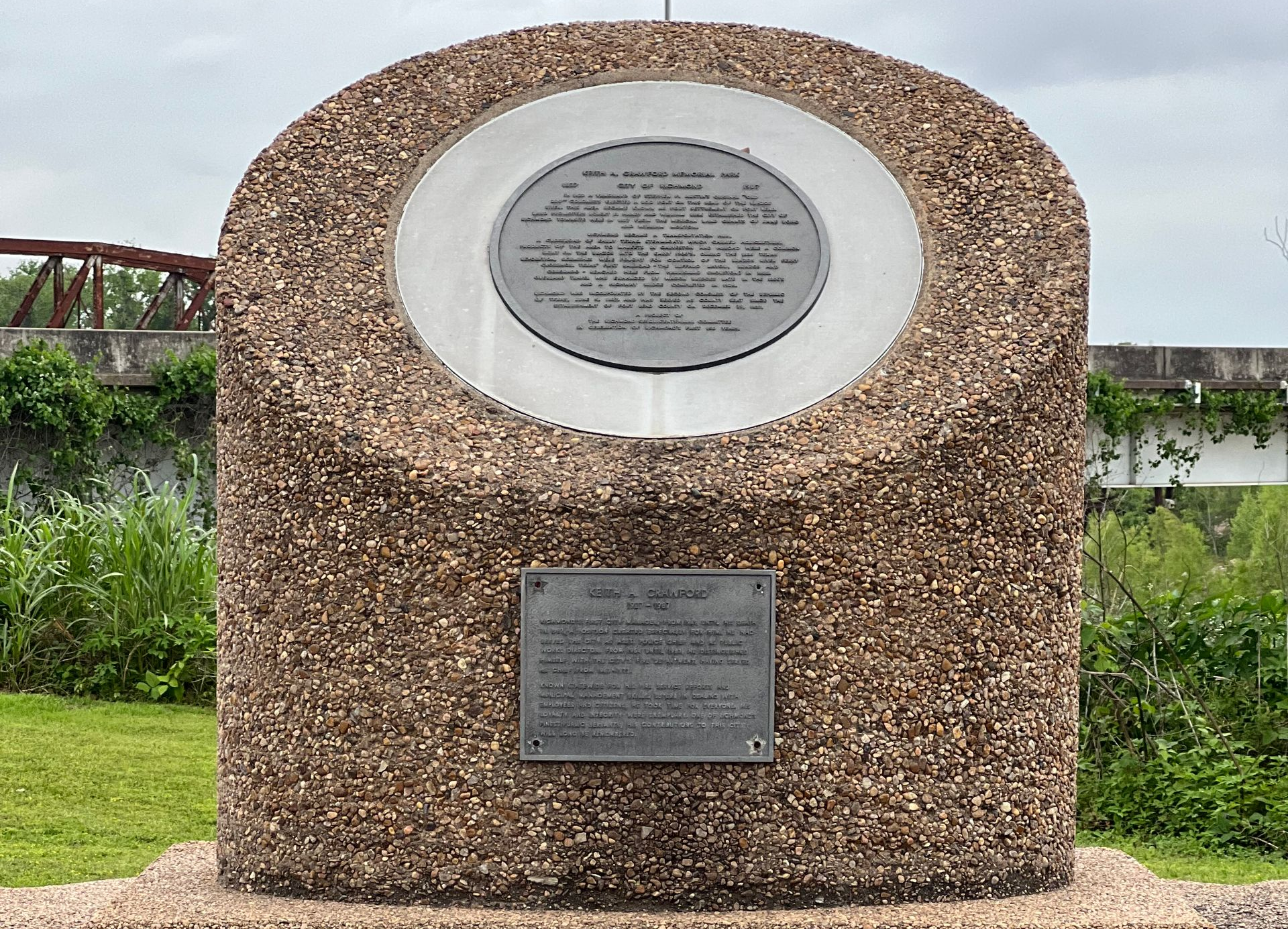 Stone memorial plaque with two plaques, set in a landscaped outdoor area.