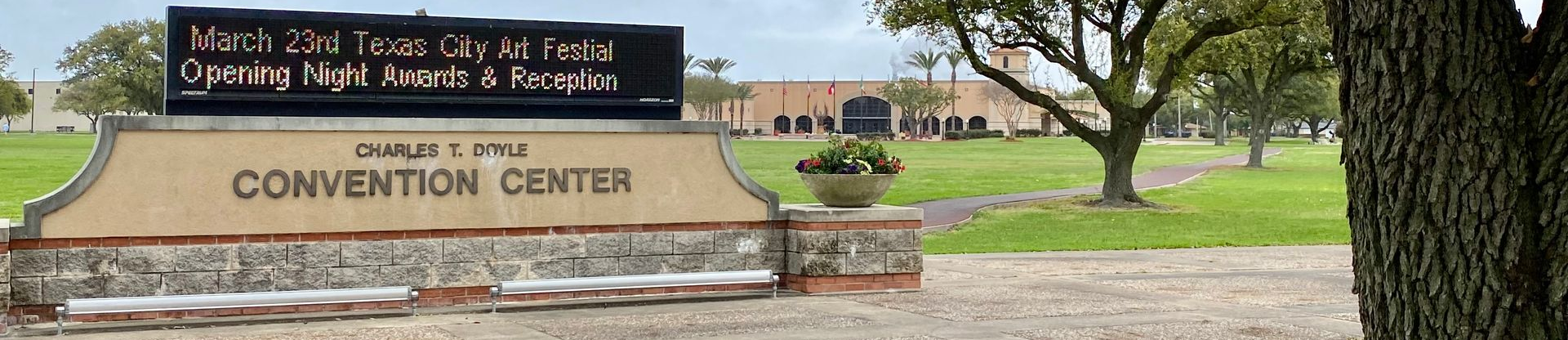Brick sign for a convention center beside a road, with grass and trees in front.