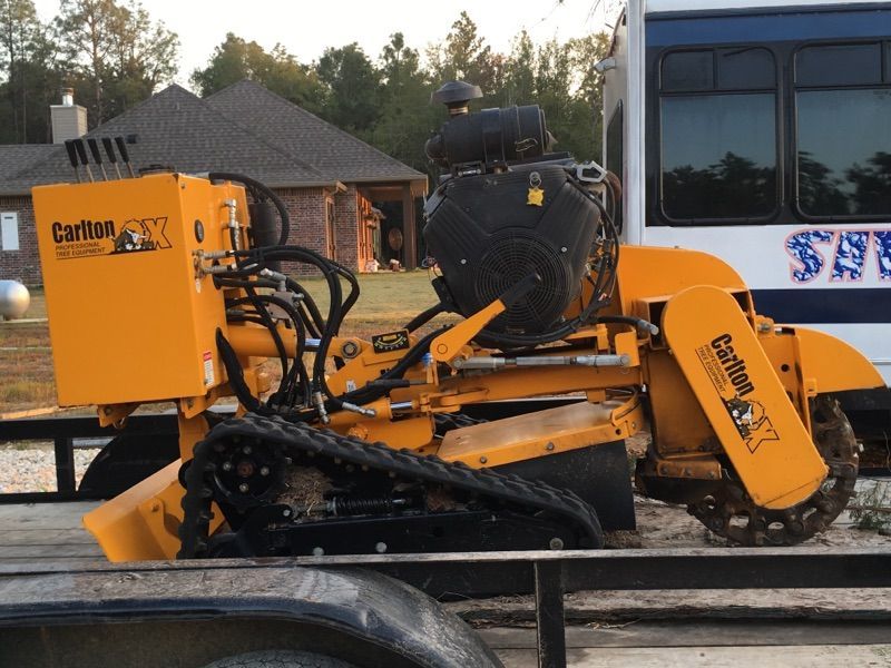 Orange road-cutting machine on a trailer at a worksite, with houses in the background.
