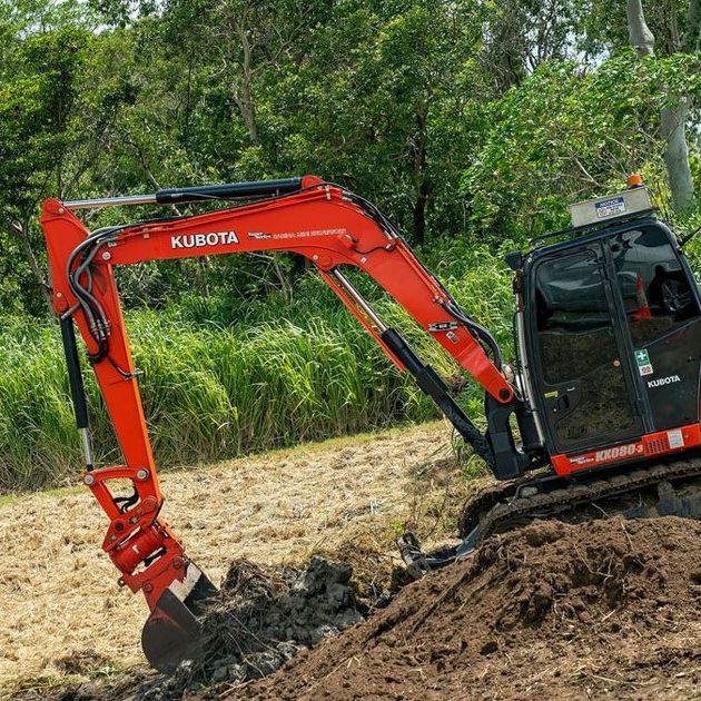 a red and black excavator is digging a hole in a field .