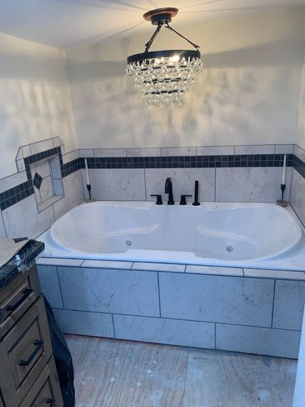 Bathroom with white tub, black fixtures, and a crystal chandelier. Tiles in black and white.
