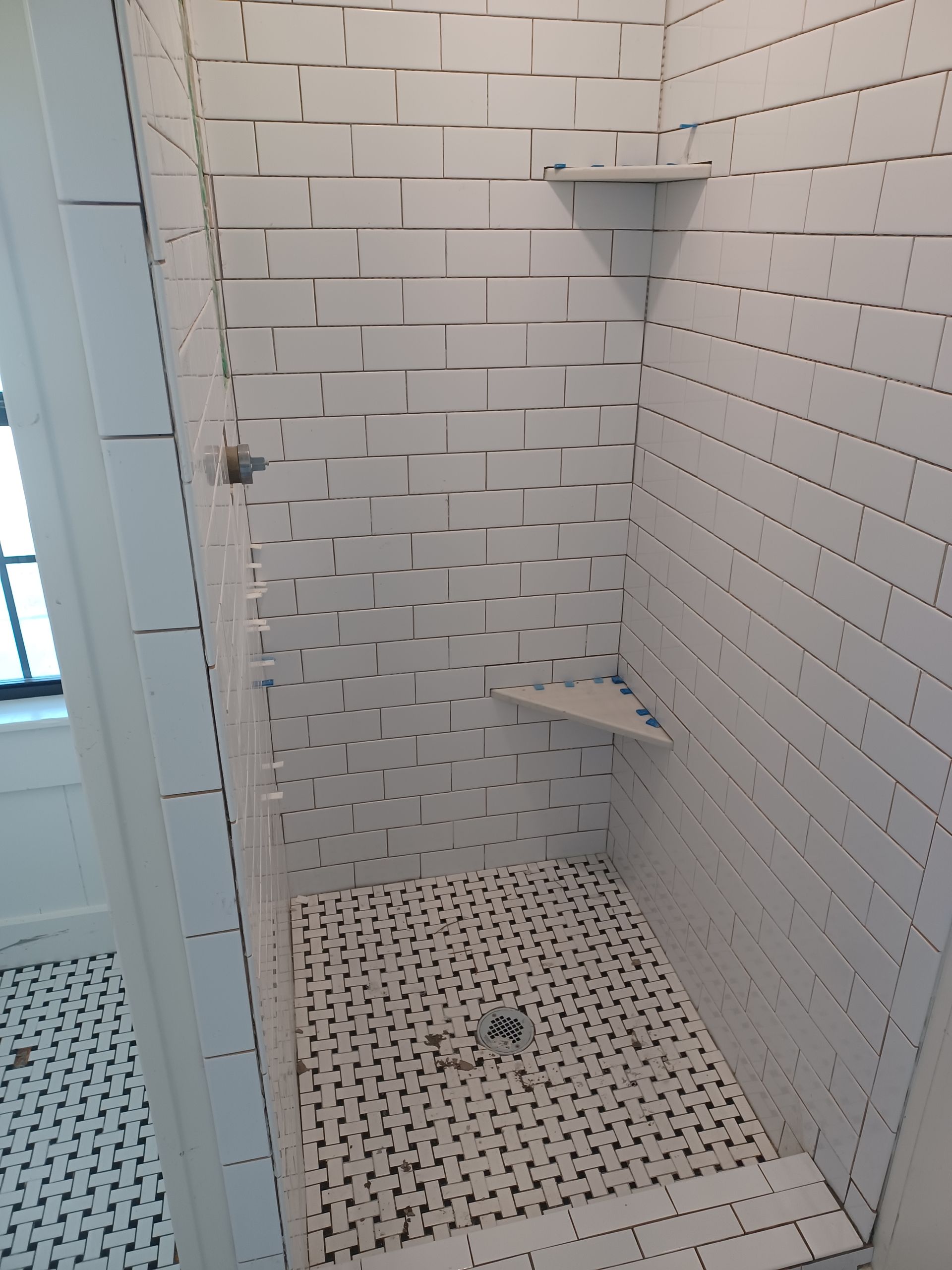 White tiled shower stall with built-in corner shelves and floor drain