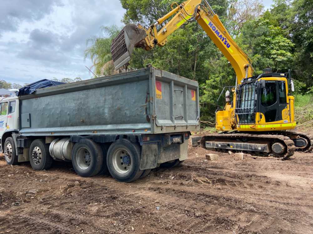 Komatsu Digger loading dirt into the bed if a truck — Allcoast Group Demolition Contractors from Gallery in Sunshine Coast, QLD Komatsu Digger loading dirt into the bed if a truck — Allcoast Group Demolition Contractors from Gallery in Sunshine Coast, QLD