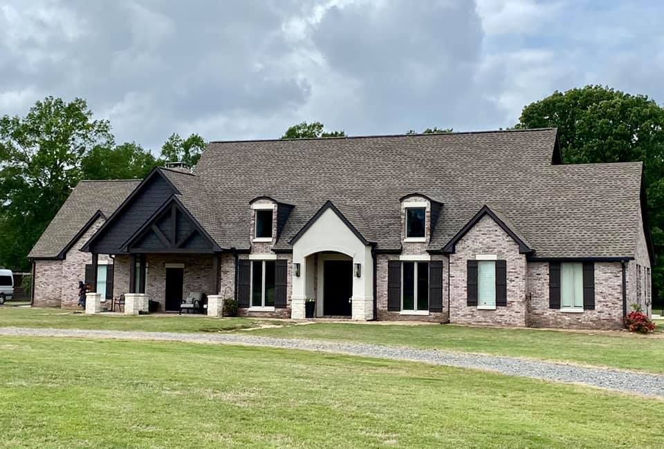 Brick house with a dark roof and shutters, a white entry, and a gravel driveway.
