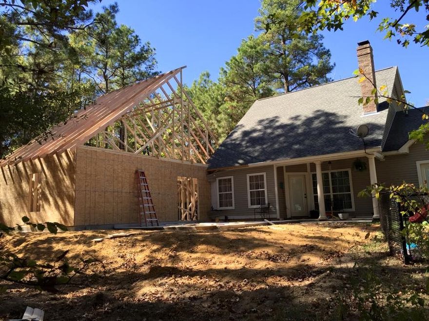 House extension under construction, new framing and sheathing visible, beside existing house.