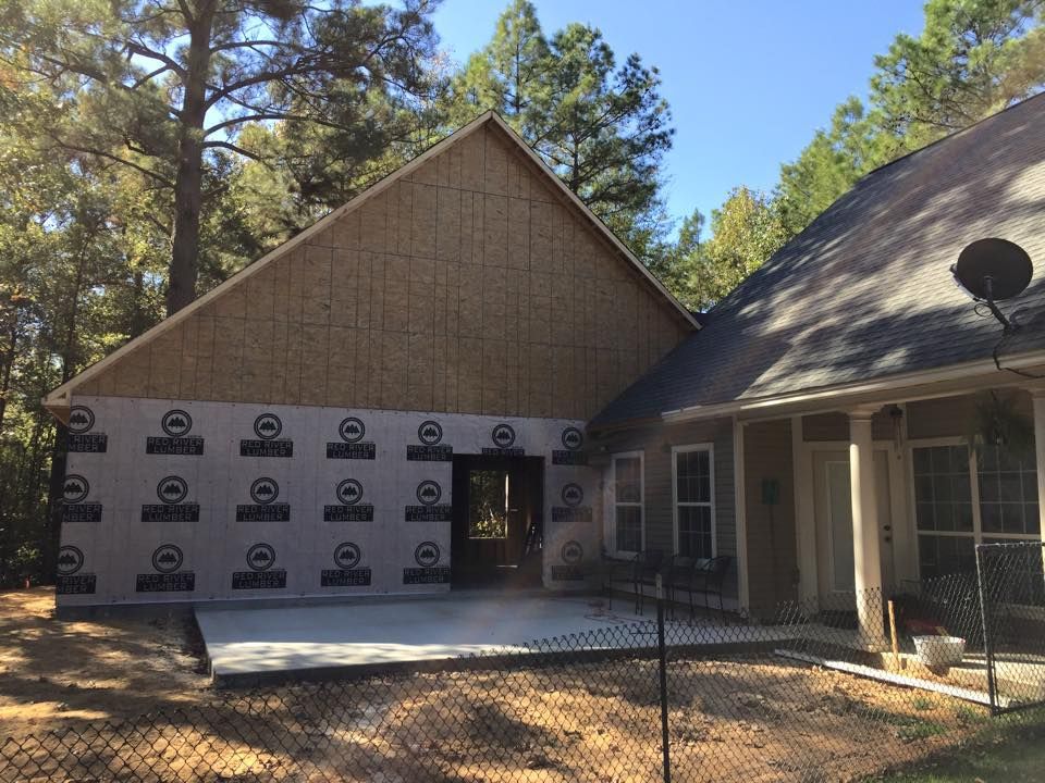 Construction site: New house addition with concrete patio, wood siding, and Tyvek wrap.