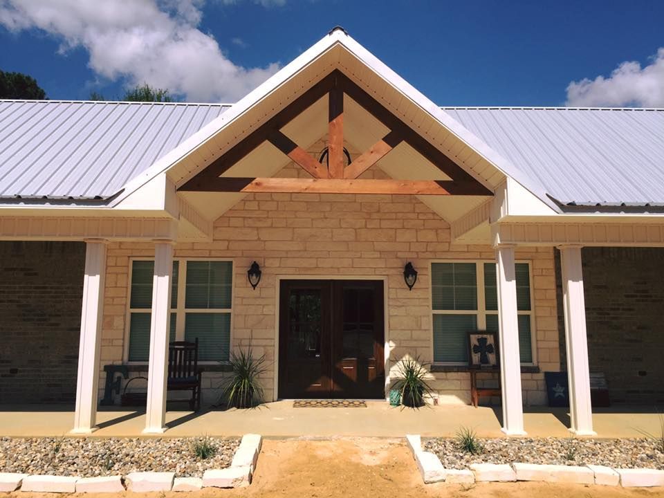 Front entrance of a light stone house with a metal roof. Brown wooden accents frame the entry door.