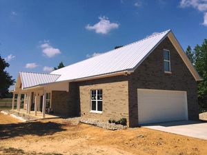 New brick house with white metal roof and garage, under a blue sky.