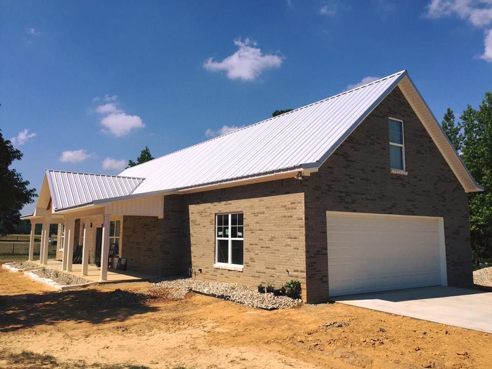 New brick house with white metal roof and garage door under a blue sky.