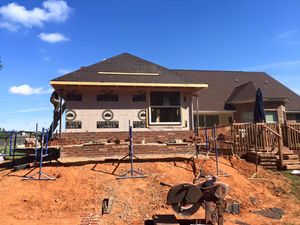 House under construction; brick foundation, siding, and roof partially completed; workers on scaffolding.