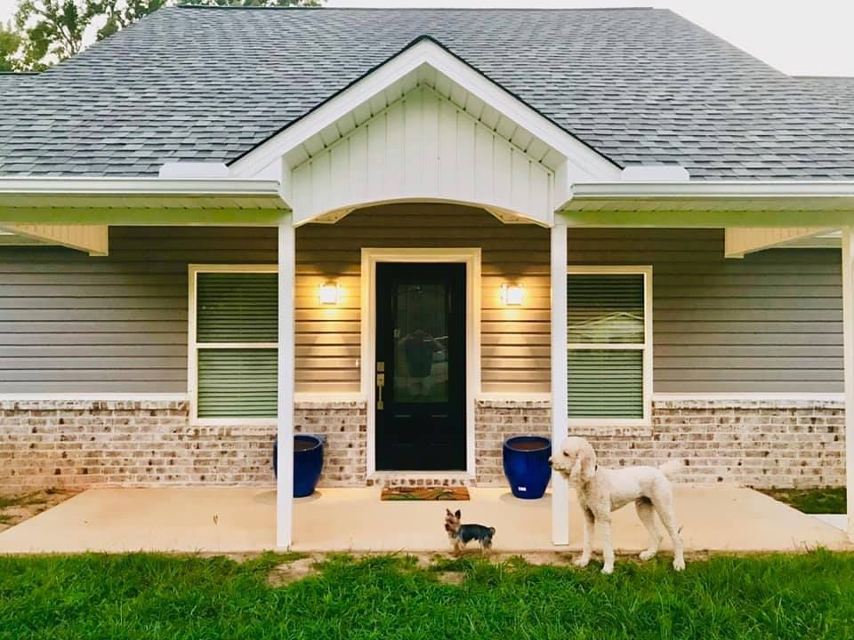 A house with a porch, two dogs, and a green yard.