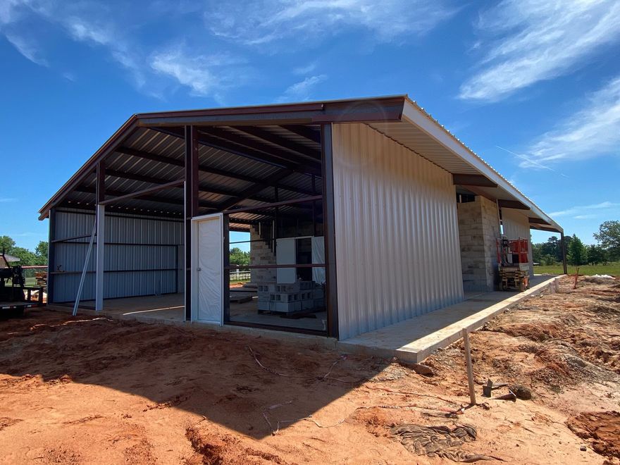 Metal barn under construction with open frame, a white door, and clear blue sky.