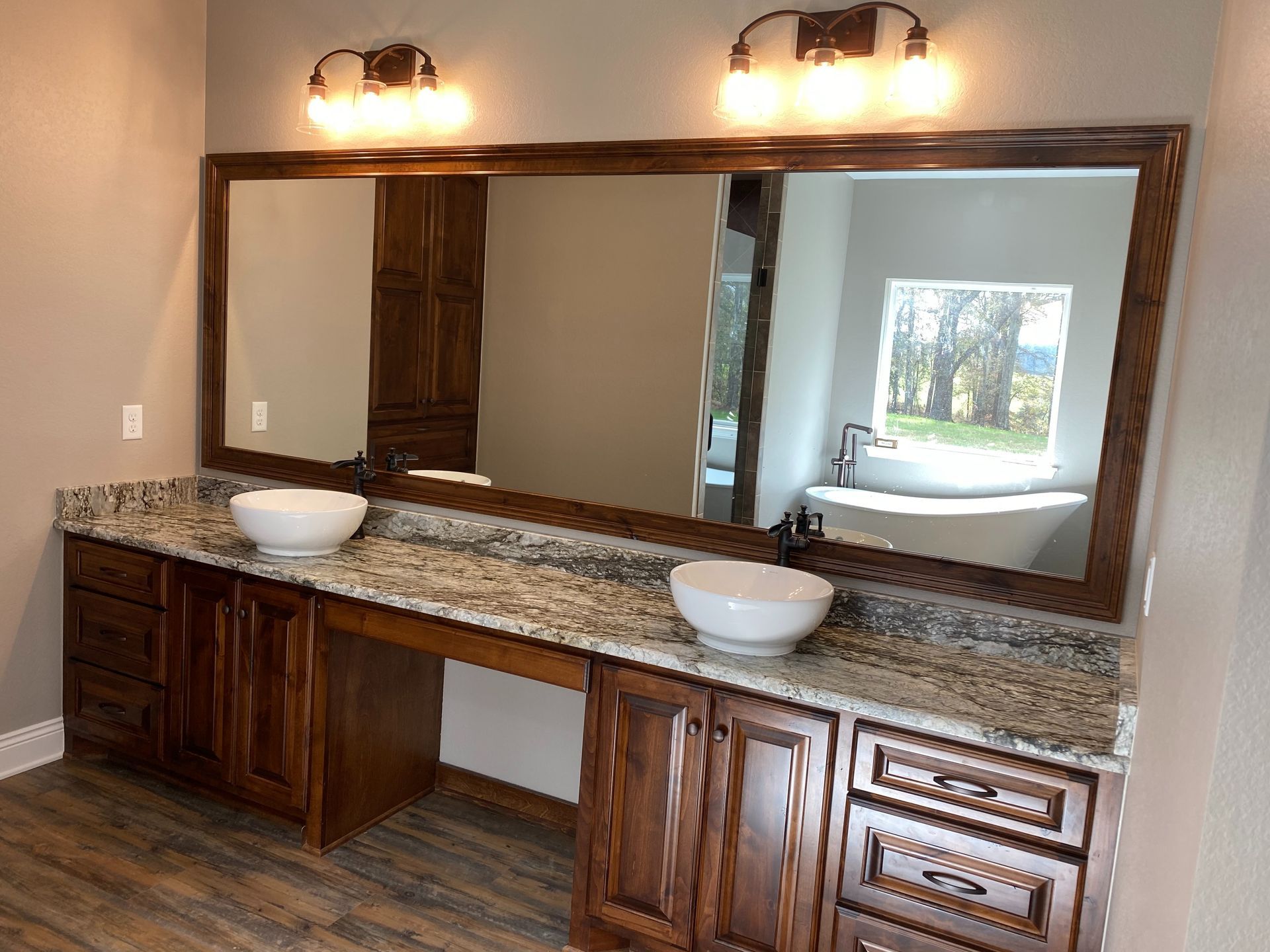 Bathroom with a large mirror, two vessel sinks, granite countertop, and wooden cabinets.