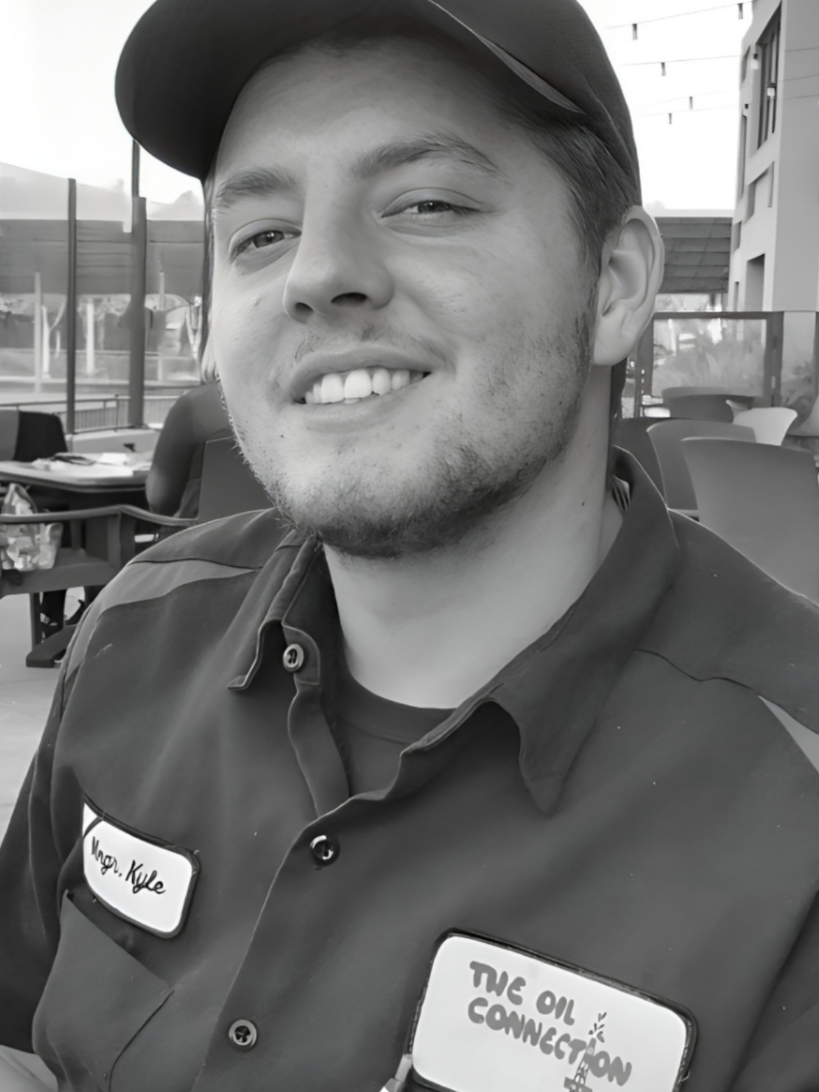 Smiling man in work shirt and baseball cap, outdoors.
