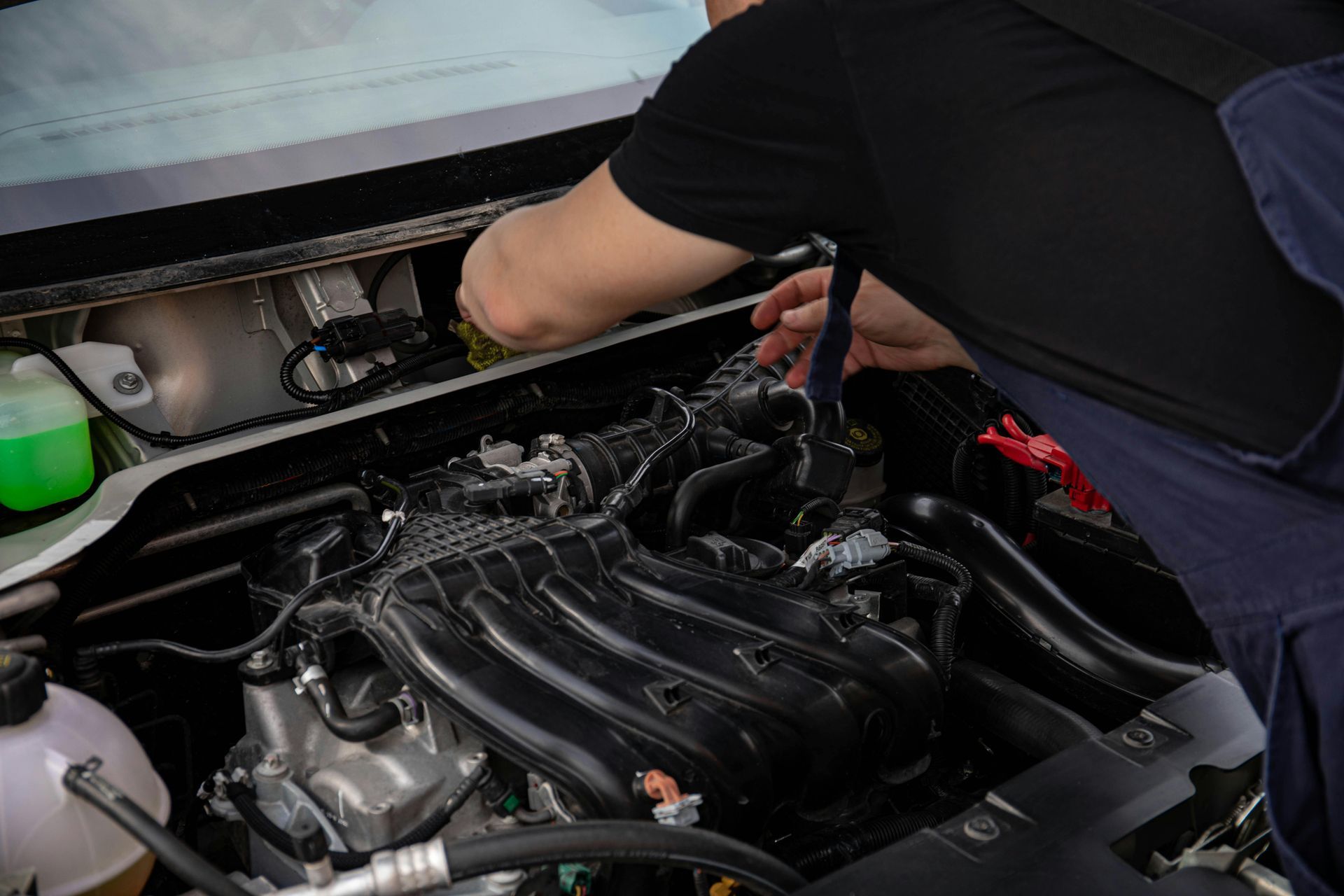 Mechanic working on a car engine, inspecting components under the hood, indoor setting.