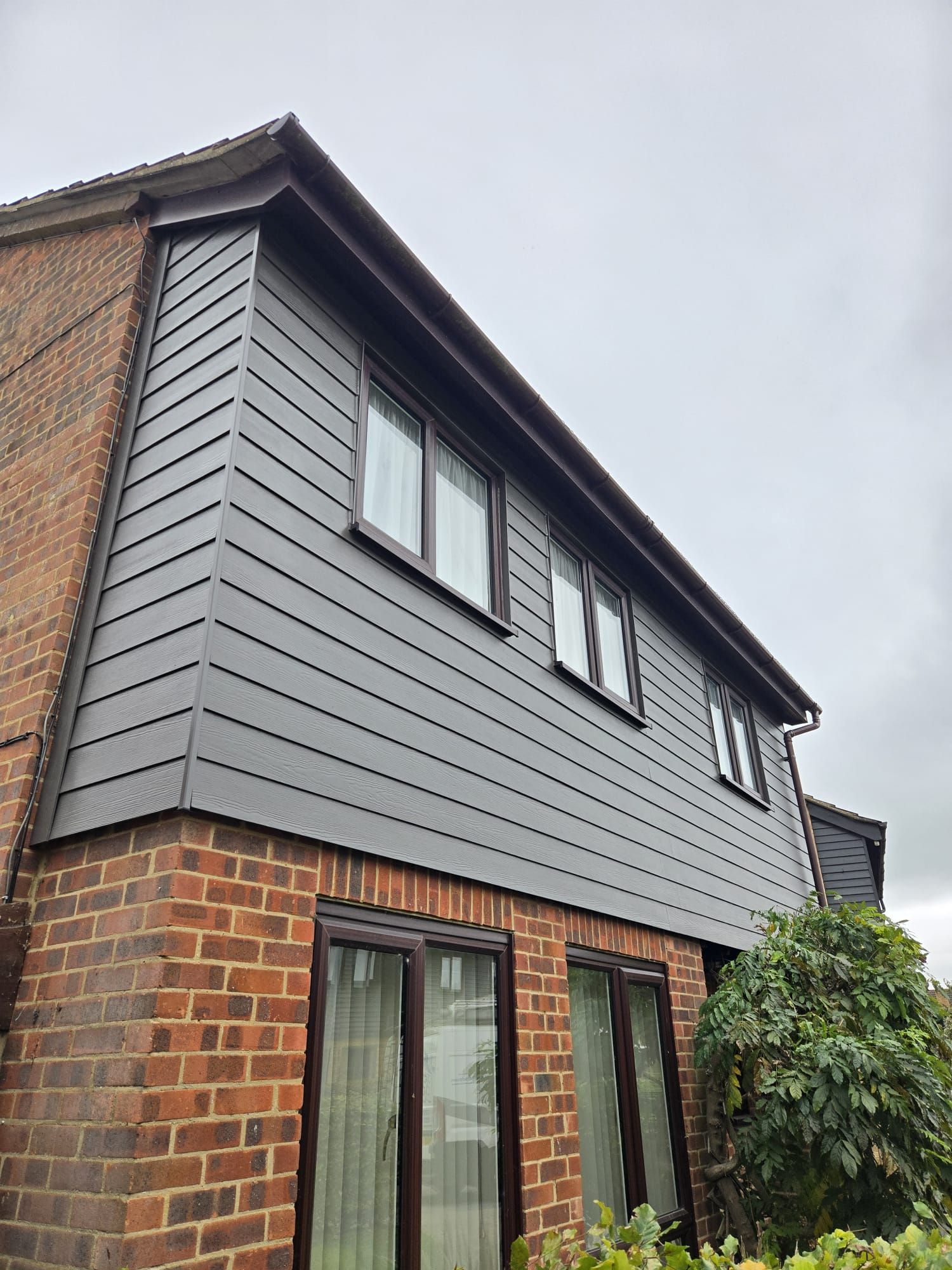 A low-angle view of a house exterior with red brick on the ground floor and grey horizontal cladding on the upper level.