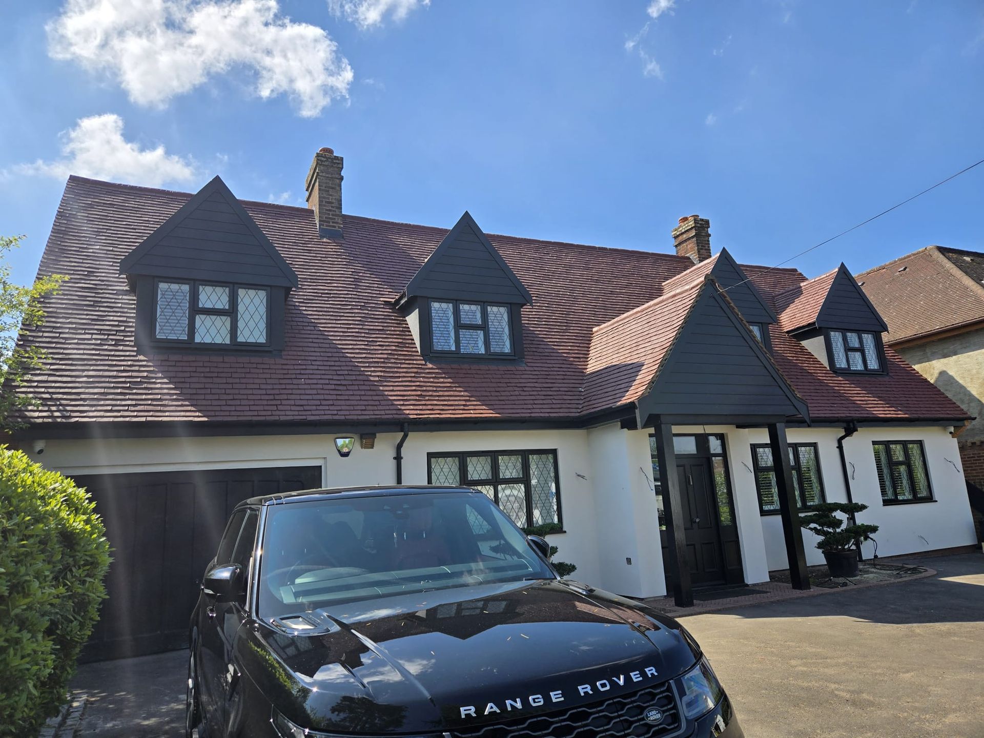 House with red roof and dormers, black Range Rover parked in front.